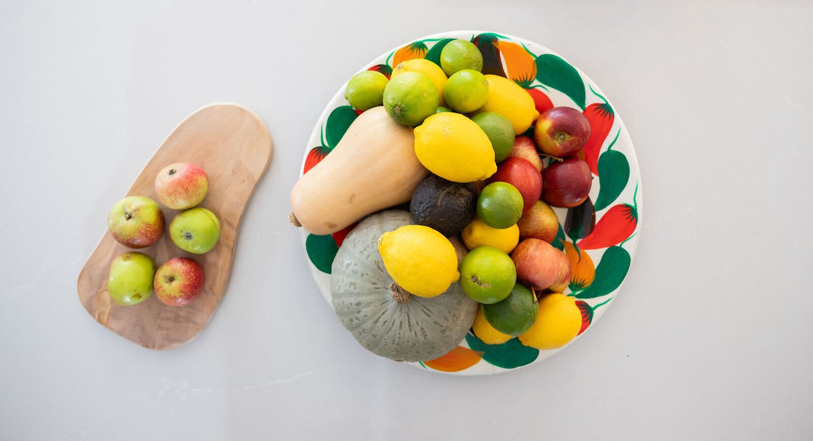 A bowl of fresh fruit and squash beside a board of apples